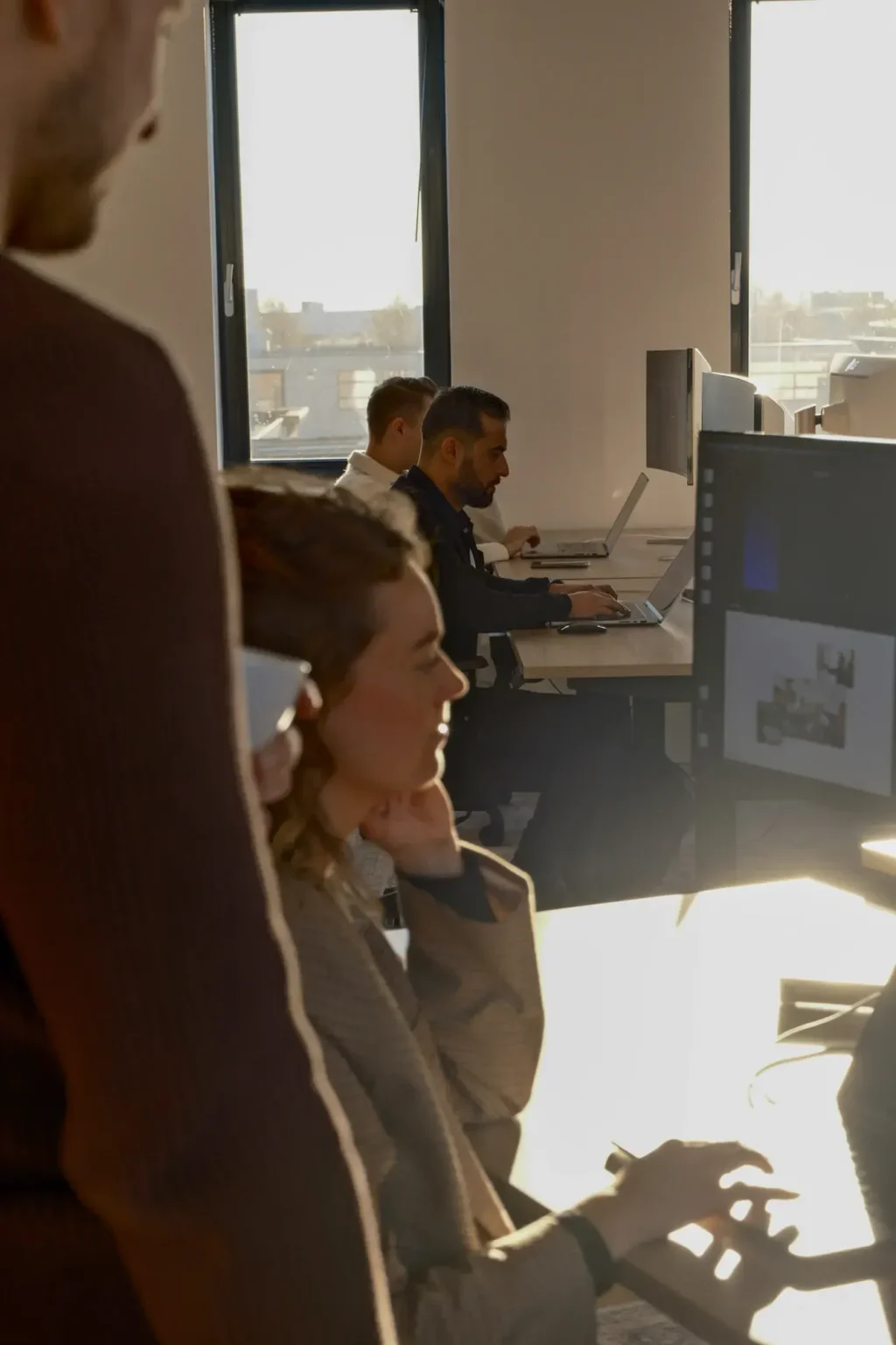 Moderne kantoorruimte met vijf mensen die geconcentreerd aan laptops en computers werken bij daglicht