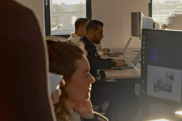 Moderne kantoorruimte met vijf mensen die geconcentreerd aan laptops en computers werken bij daglicht