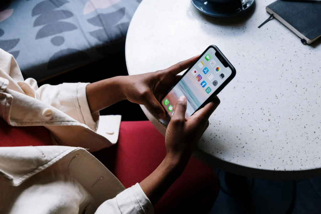 Persoon met lichte jas en roze broek houdt smartphone vast aan ronde tafel met notitieboekje en kopje
